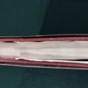 May include: Close-up of the spine of a hardback book with a red and black cover. The book is closed and the spine is visible.
