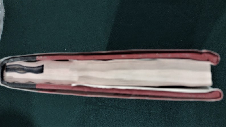 May include: Close-up of the spine of a hardback book with a red and black cover. The book is closed and the spine is visible.
