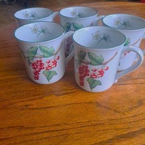 May include: A set of five white ceramic mugs with a green rim and handle. Each mug features a design of red berries and green leaves on a branch. The top of each mug has a floral design.