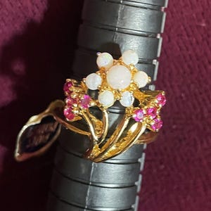 May include: A gold ring with a cluster of white opals in the center and pink stones surrounding the base of the ring.
