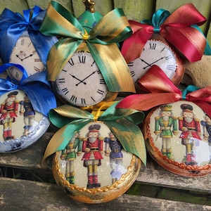 Könnte beinhalten: Dekorative Weihnachtskugeln mit Uhren-Zifferblättern mit römischen Ziffern und Spielzeugsoldaten-Motiven. Jede Kugel ist mit einer großen, farbenfrohen Schleife in Blau-, Grün- und Rottönen verziert. Die Kugeln liegen auf einer Holzoberfläche.