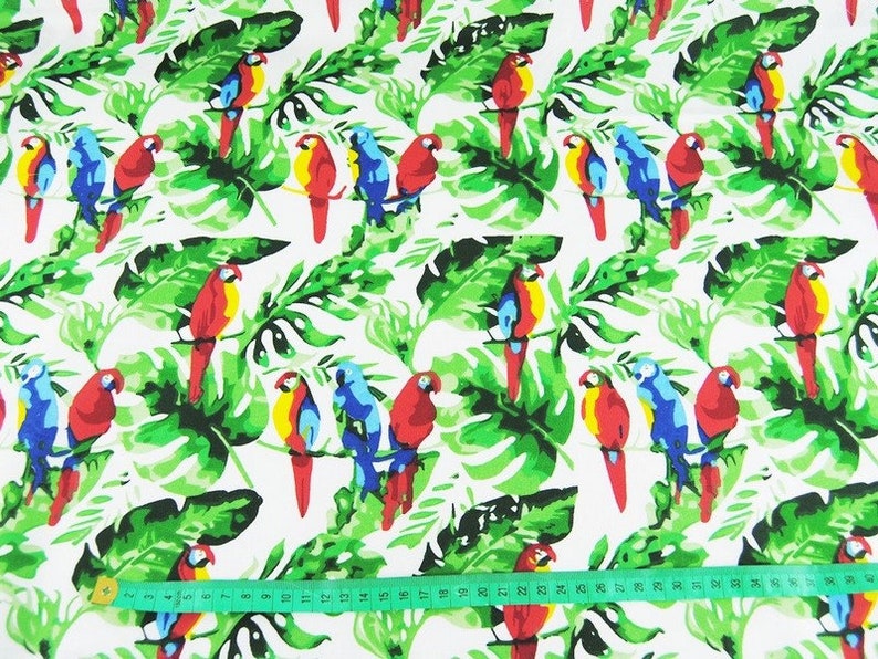 May include: White fabric with a repeating pattern of colorful parrots and green tropical leaves. The fabric is measured with a tape measure.