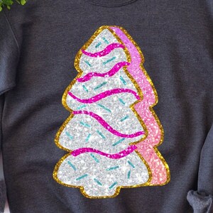 May include: A grey sweatshirt featuring a sparkly silver, pink and gold Christmas tree design. The tree has pink and white frosting and blue sprinkles.