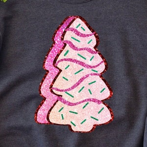 May include: A pink and white glitter Christmas tree with green sprinkles. The tree is on a dark grey background.