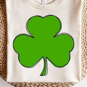 May include: A white t-shirt featuring a green shamrock design. The shamrock is outlined in black and white.