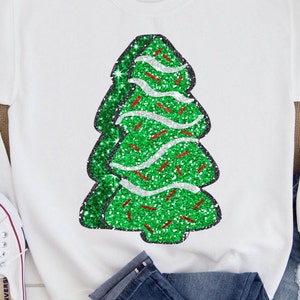 Pode incluir: Camisola branca com um design de árvore de Natal de glitter verde. A árvore tem detalhes de glitter vermelho e branco.