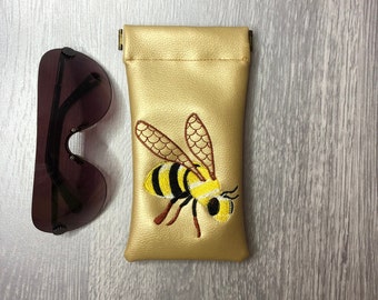 Embroidered bumble bee glasses case. Gold coloured faux leather flex spring closing case.