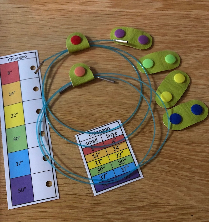 May include: Three sets of turquoise circular knitting needles with green, yellow, blue, red, and purple colored caps. The needles are laid out on a wooden surface with a chart showing the sizes of the needles in inches.