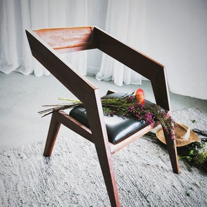 May include: A dark brown wooden chair with a black leather seat. The chair is angled and has a unique geometric design. A bouquet of pink flowers is resting on the seat.