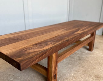 May include: A wooden coffee table with a natural wood finish and a simple, rectangular design. The table has a wide, flat top and a sturdy base with four legs.