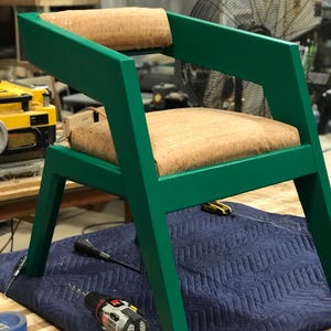 May include: A green chair with a cork seat and back. The chair has a unique angled design and is sitting on a blue work surface.