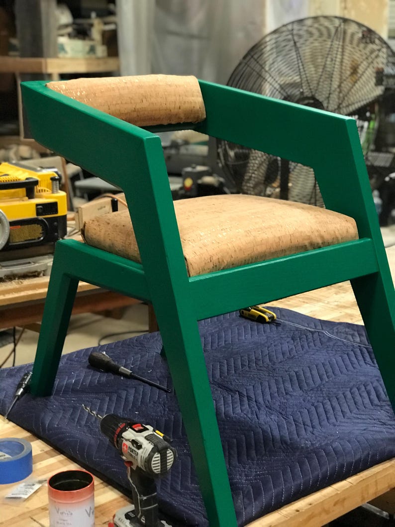 May include: A green chair with a cork seat and back. The chair has a unique angled design and is sitting on a blue work surface.