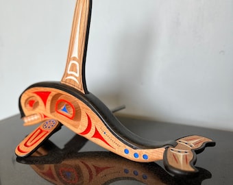 May include: A wooden carving of an orca whale with red, white, and blue accents. The orca is in a leaping position with its tail raised. The carving is made of different types of wood and has a black base.