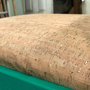 May include: A close-up of a green chair with a cork seat. The cork is a natural material with a light brown color and a slightly textured surface.