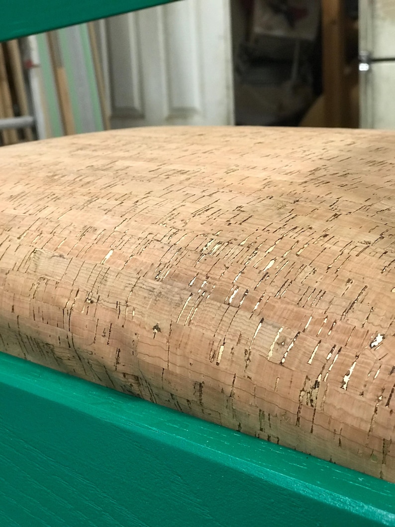 May include: A close-up of a green chair with a cork seat. The cork is a natural material with a light brown color and a slightly textured surface.