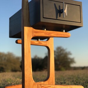 May include: A black wooden nightstand with a single drawer and a modern metal handle. The nightstand is on a wooden stand with a unique curved design.