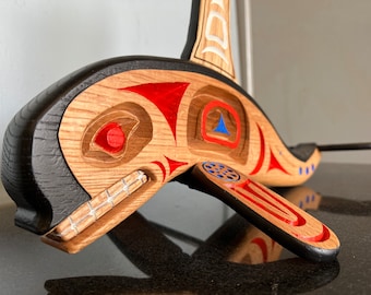May include: A wooden carving of an orca whale with red, blue, and white paint details. The orca is carved in a traditional style with geometric patterns.