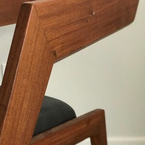 May include: A wooden chair with a dark brown finish and a black fabric seat. The chair has a unique angled design with a sharp, geometric shape.