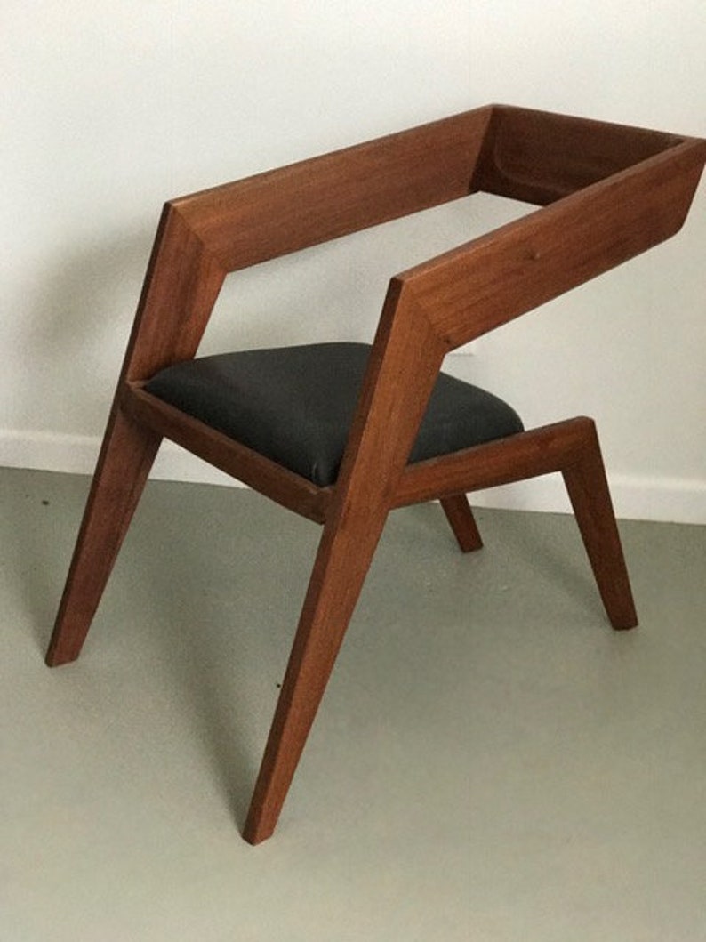 May include: A wooden chair with a dark gray fabric seat. The chair has a unique, angular design with a high back and angled legs.