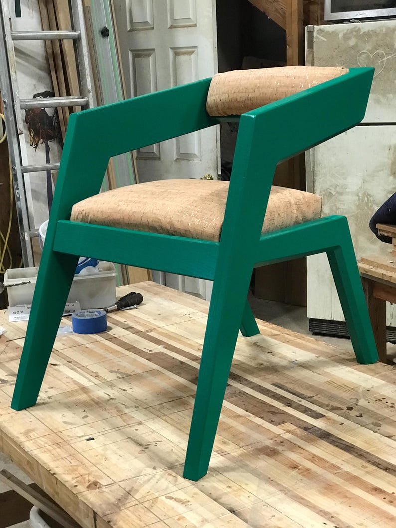 May include: A green chair with a cork-covered seat and back. The chair has a unique, angular design with a wide, flat back and angled legs.