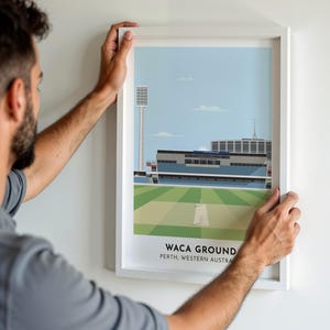 May include: A framed illustration of the WACA Ground in Perth, Western Australia. The illustration shows the stadium and the cricket pitch. The frame is white and the illustration is in a cartoon style.
