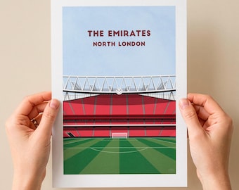 May include: A rectangular art print featuring a graphic illustration of The Emirates stadium in North London. The image displays a green soccer field, red stadium seating, a white roof structure, and a light blue sky with the text THE EMIRATES NORTH LONDON.