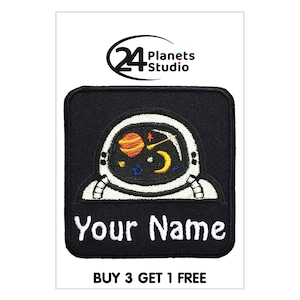 Puede incluir: Parche termoadhesivo negro con un astronauta que lleva un casco con planetas y estrellas en su interior. El texto "Your Name" está debajo del astronauta. El texto "BUY 3 GET 1 FREE" está debajo del parche.