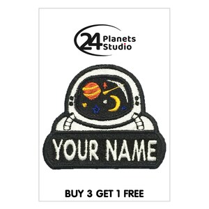 May include: Embroidered iron-on patch featuring a cartoon astronaut with a planet, moon, and stars in the helmet. The patch has a black background with white text that says "YOUR NAME".