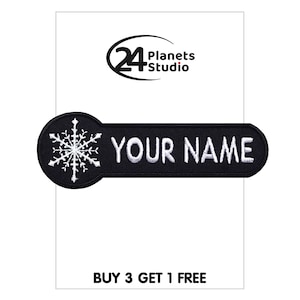 Op de afbeelding: Zwart-witte strijkpatch met een sneeuwvlokdesign en de tekst "YOUR NAME". De patch is op een witte achtergrond met de tekst "24 Planets Studio" en "BUY 3 GET 1 FREE" boven en onder.