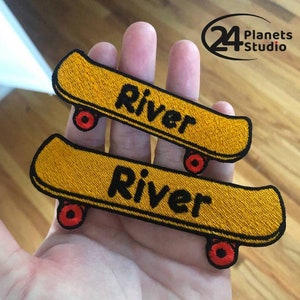 May include: Two yellow embroidered iron-on patches shaped like skateboards with the name "River" in black lettering.