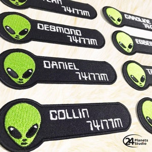 Peut inclure: Patchs thermocollants brodés noirs et verts avec des têtes d'extraterrestres et des noms, dont 'Collin', 'Daniel', 'Debmono' et 'Caroline'. Chaque patch comporte un numéro blanc '74177M' imprimé dessus.