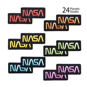 May include: Set of ten iron-on patches featuring the NASA logo in various colours, including red, orange, yellow, green, blue, and pink. The patches are arranged in pairs, with each pair featuring the same colour. The patches are all rectangular in shape and have a black background.