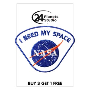Pode incluir: Etiqueta bordada azul e branca com o texto "I need my space" e o logotipo da NASA. A etiqueta tem um fundo branco e costuras azuis. O texto "BUY 3 GET 1 FREE" está na parte inferior da imagem.