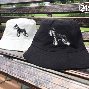 Puede incluir: Dos sombreros de pescador con una imagen bordada de un perro schnauzer miniatura. Un sombrero es blanco y el otro es negro.