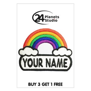 Puede incluir: Parche bordado con un arcoíris en rojo, naranja, amarillo, verde, azul y morado. Tiene una pancarta blanca con el texto "YOUR NAME" en negro. Incluye dos nubes blancas y el texto "BUY 3 GET 1 FREE".