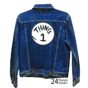 Könnte beinhalten: Eine blaue Jeansjacke mit einem weißen Kreis-Patch auf der Rückseite, auf dem in schwarzen Buchstaben "Thing 1" steht.