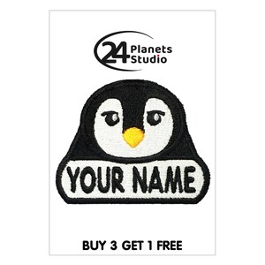 May include: Black and white penguin cartoon iron-on patch with the text "YOUR NAME" in white. The patch is for clothing or fabric.  The patch is from 24 Planets Studio.