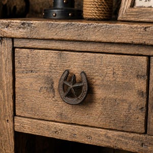 May include: A rustic brown wooden drawer featuring a dark metal pull shaped like a horseshoe with a five-pointed star in the centre. The wood has a weathered, textured grain finish, and the drawer is set within a matching wooden frame structure.