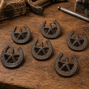May include: Six dark brown cast iron decorative accents, each shaped like a horseshoe with a five-pointed star centered within the arch. These metal pieces feature a textured, rustic finish and are arranged in a cluster on a wooden surface.