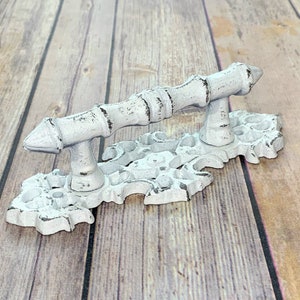 May include: White cast iron door pull with a decorative, ornate base and a simple, straight handle.