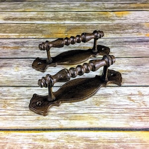 May include: Two rustic brown cast iron drawer pulls with a decorative scroll design and a beaded handle.