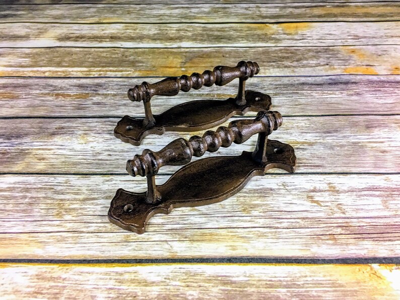 May include: Two rustic brown cast iron drawer pulls with a decorative scroll design and a beaded handle.