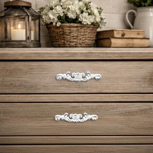 Könnte beinhalten: Ein Set aus drei Keramikbechern mit gesprenkelter, matter Oberfläche. Die Becher sind in Creme-, Hellgrau- und Dunkelgrautönen gehalten. Jeder Becher hat ein schlichtes, modernes Design und einen abgerundeten Griff.