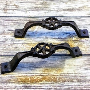 Può includere: Due maniglie per porte in ghisa nera con un design a stella. Le maniglie sono curve e hanno una finitura rustica.