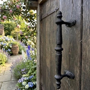 May include: A black, cast iron door handle with a vertical, spindle-shaped design featuring decorative rounded accents. The handle is mounted onto a weathered, dark brown wooden door with visible vertical grain and metal hinges.
