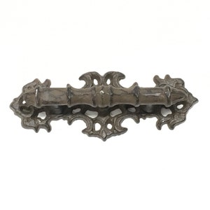 Puede incluir: Un tirador de caj&oacute;n de hierro fundido con un dise&ntilde;o decorativo y ornamentado. El tirador tiene un acabado marr&oacute;n oscuro y una forma rectangular.