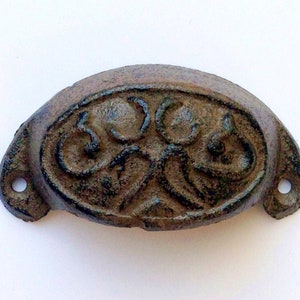 May include: A cast iron drawer pull with a decorative, ornate design. The pull is dark brown and has a slightly distressed finish.