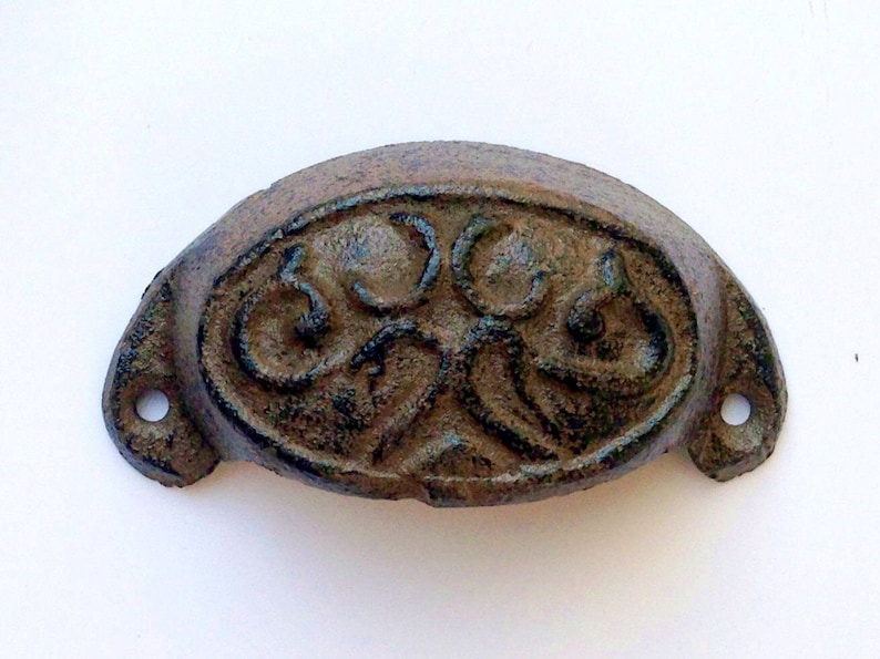 Może przedstawiać: Metalowy uchwyt do szuflady wykonany z żeliwa, z ozdobnym, bogatym wzorem. Uchwyt jest ciemnobrązowy i ma lekko postarzaną powierzchnię.