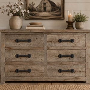 May include: A rectangular wooden dresser featuring six drawers arranged in two columns. Each drawer is equipped with a dark, textured metal handle. The wood has a weathered, light brown finish with visible grain patterns and a rustic, natural appearance.