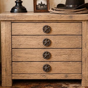 May include: A light brown wooden nightstand featuring four horizontal drawers, each equipped with a dark metal star-shaped knob. The piece has a rectangular top surface and a textured wood grain finish, providing a sturdy and functional storage unit.